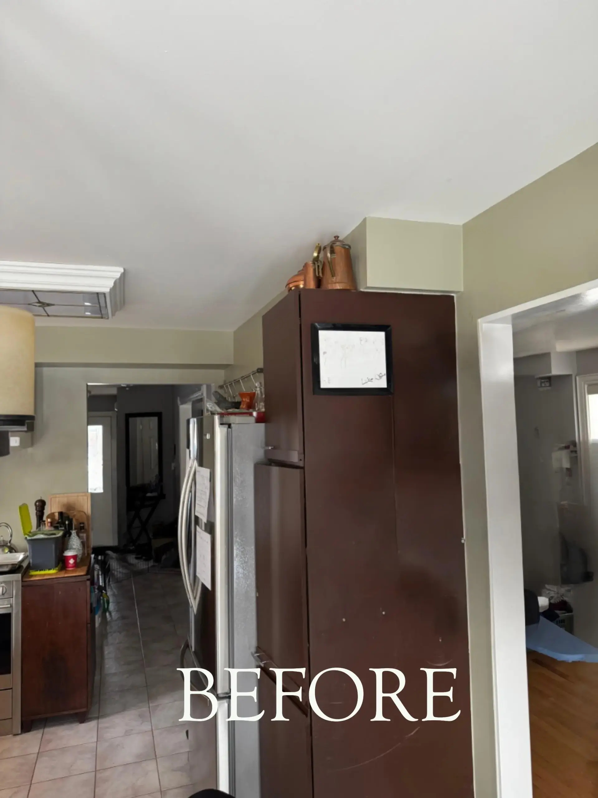 Kitchen with a tall dark cabinet, stainless steel fridge, and the word BEFORE overlaid near the bottom