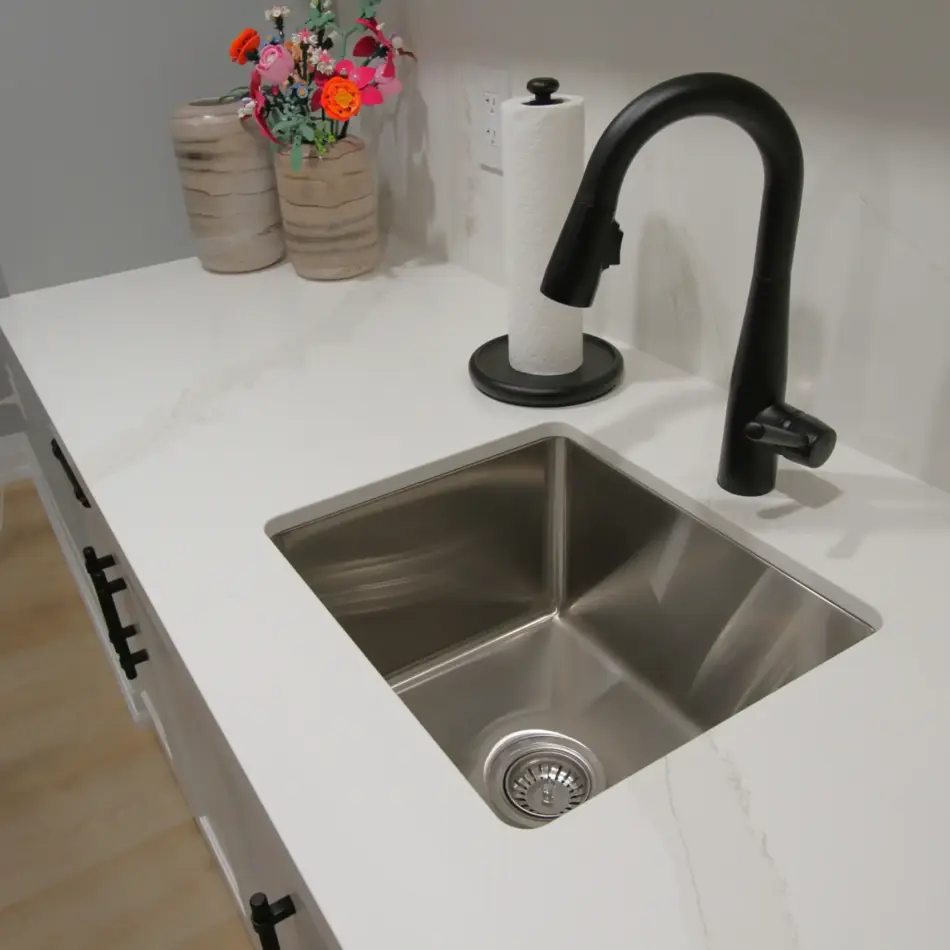 IMG_3950 Modern kitchen sink with a black faucet, white countertop, paper towel roll, and decorative vases with flowers