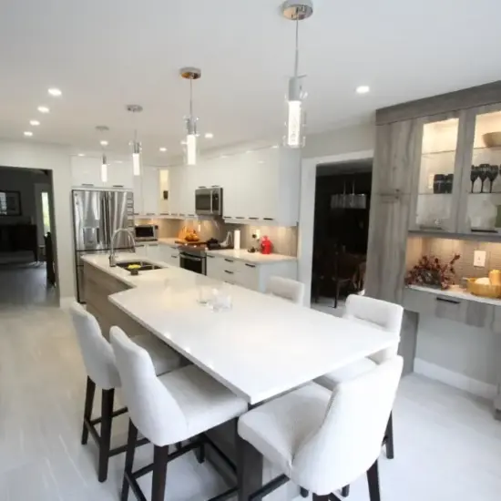 Modern white kitchen with a large island, four stools, pendant lights, stainless steel appliances, and gray built-in cabinets