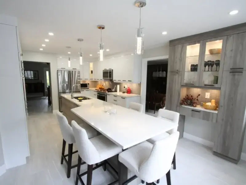 Modern white kitchen with a large island, four stools, pendant lights, stainless steel appliances, and gray built-in cabinets