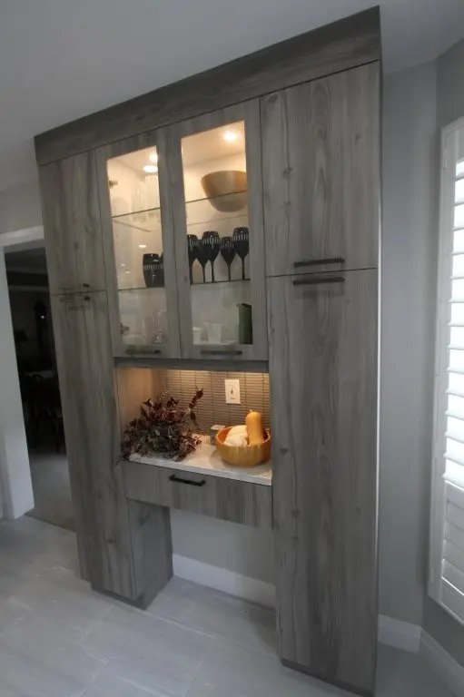 Built-in kitchen pantry cabinet with glass-front upper doors, under-cabinet lighting, and an open counter shelf