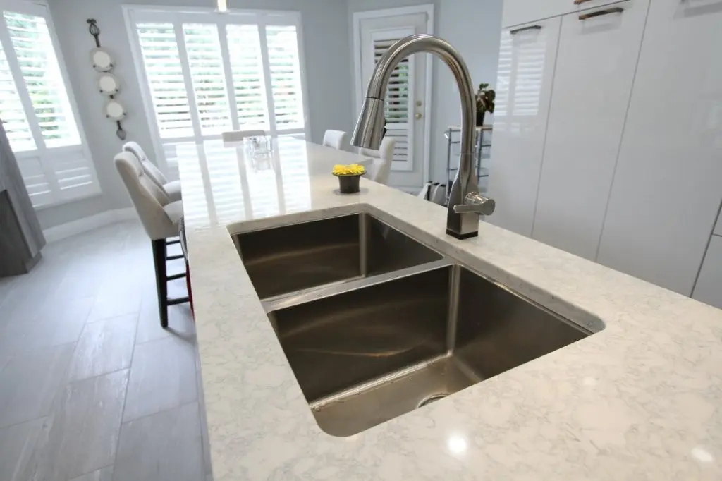 Modern kitchen island with double stainless-steel sink, faucet, and bar seating in a bright white kitchen