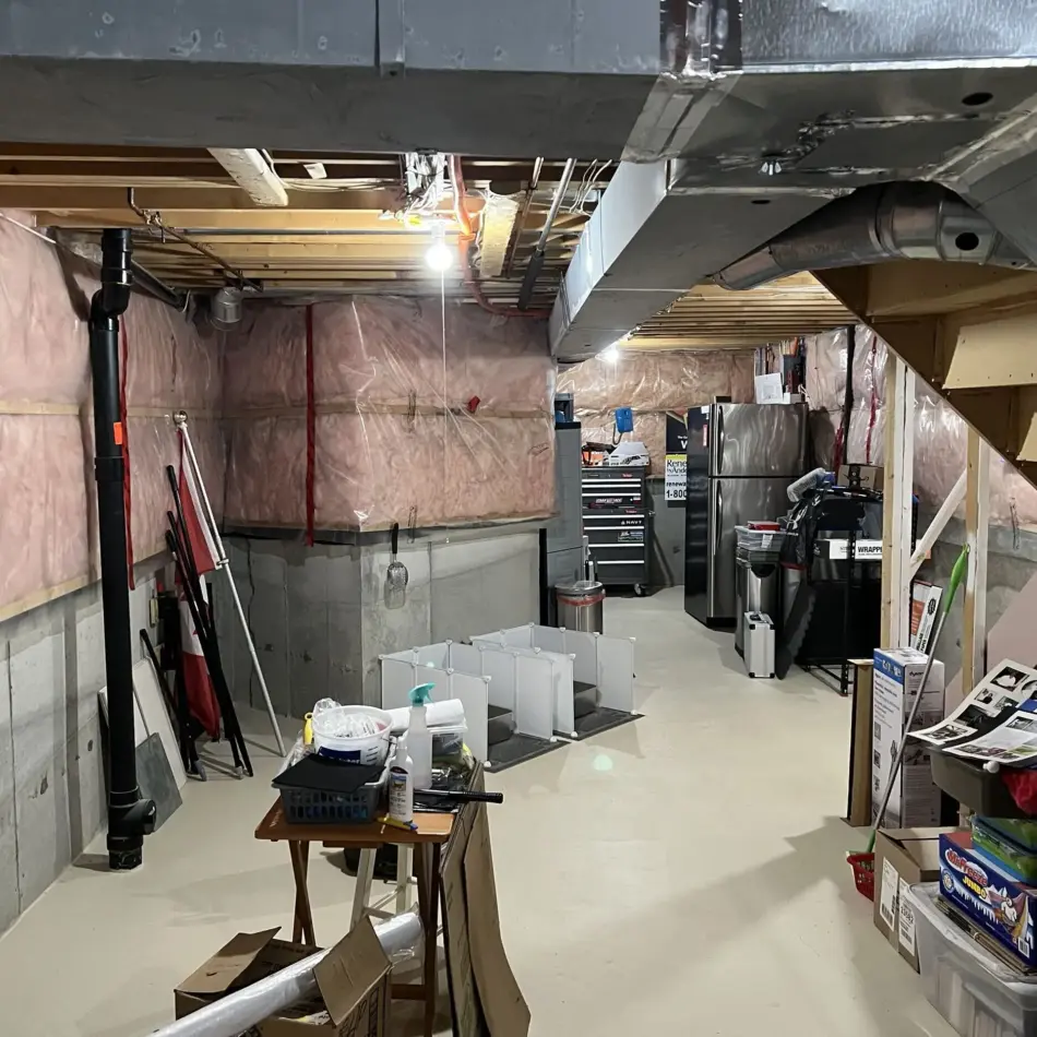 IMG_7672 Unfinished basement with exposed ceiling beams, ductwork, pink insulation, storage items, and a staircase on the right