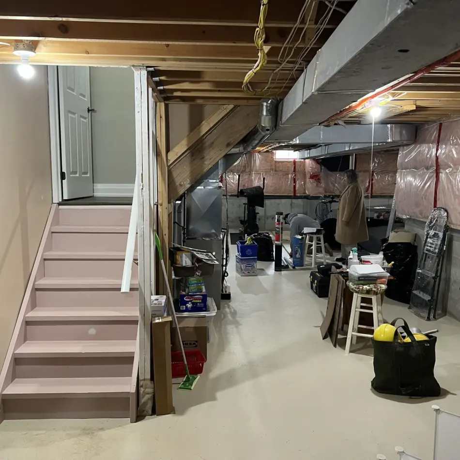 IMG_7677 Partially finished basement with pink stairs, exposed joists and ducts, plastic-covered walls, and people working inside