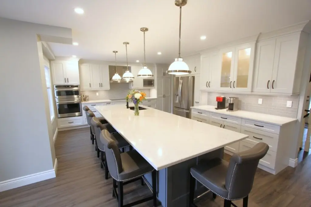 Modern white kitchen with a large island, pendant lights, and bar stools