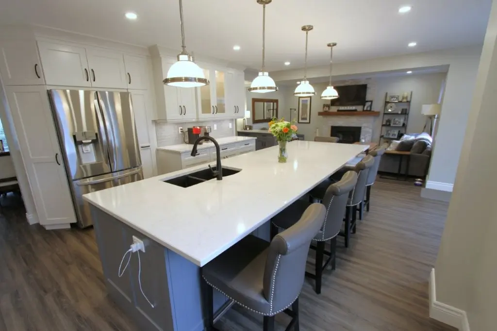 Modern open-concept kitchen with a large island, stainless refrigerator, and bar seating, opening to a living room with a fireplace