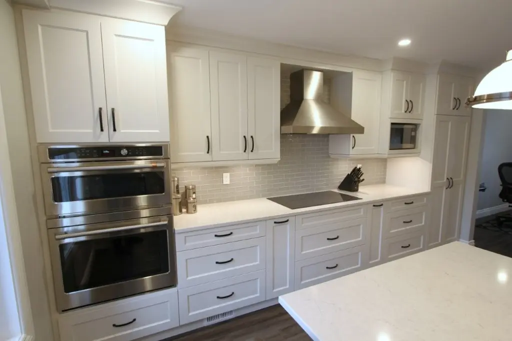 Modern white kitchen with stainless steel double wall oven, range hood, and built-in microwave