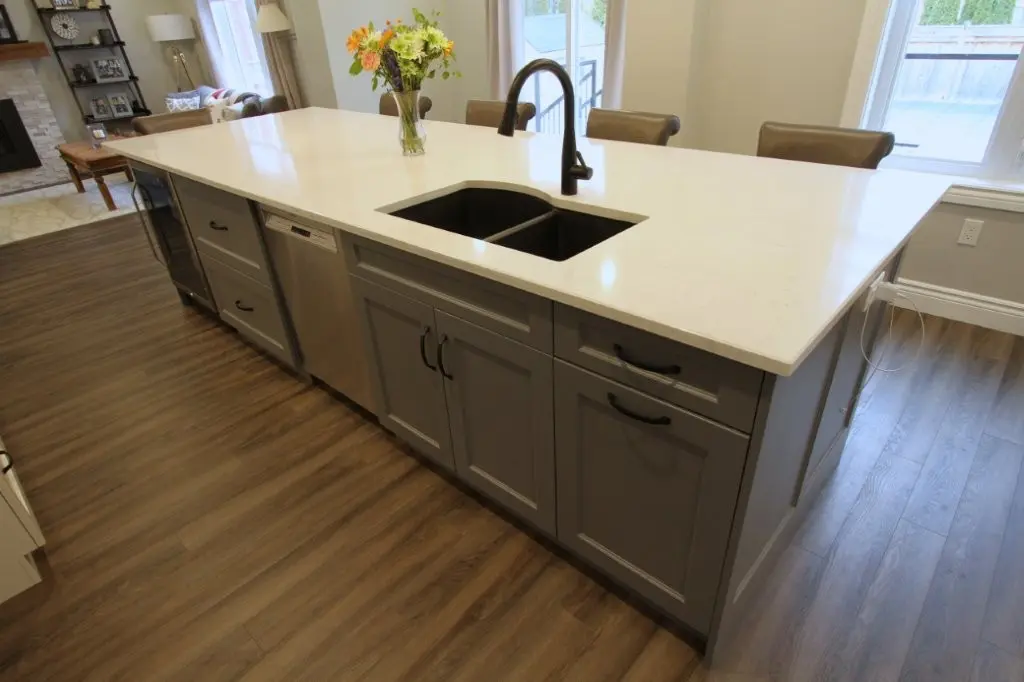 Kitchen island with white countertop, double sink, and dark cabinets in a bright open room